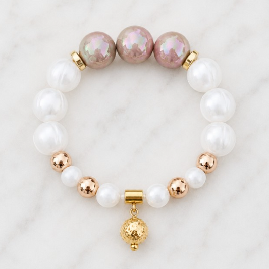 Handmade Morning Dew bracelet featuring white silicone beads, pearlescent ivory accent beads, polished gold Hematite beads and a gold pendant on a white marble background.