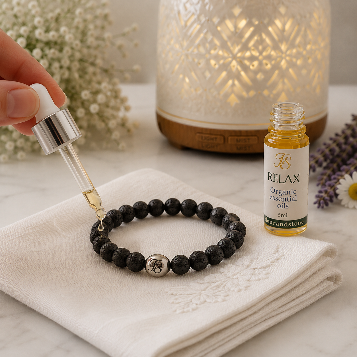 Applying Fleur & Stone Relax Essential Oil Blend to a black lava bead aromatherapy bracelet resting on a white cloth before wearing.