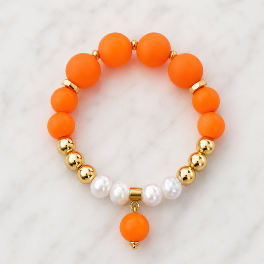 Handmade Sunset Glow bracelet featuring matte orange and white silicone beads, polished gold Hematite accents and an orange pendant charm on a white marble background.