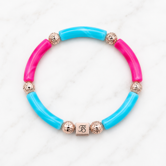 Pink Lagoon Bracelet by Fleur & Stone featuring turquoise and pink acrylic tube beads, textured rose gold lava beads and a rose gold stainless steel logo bead on a white marble background.
