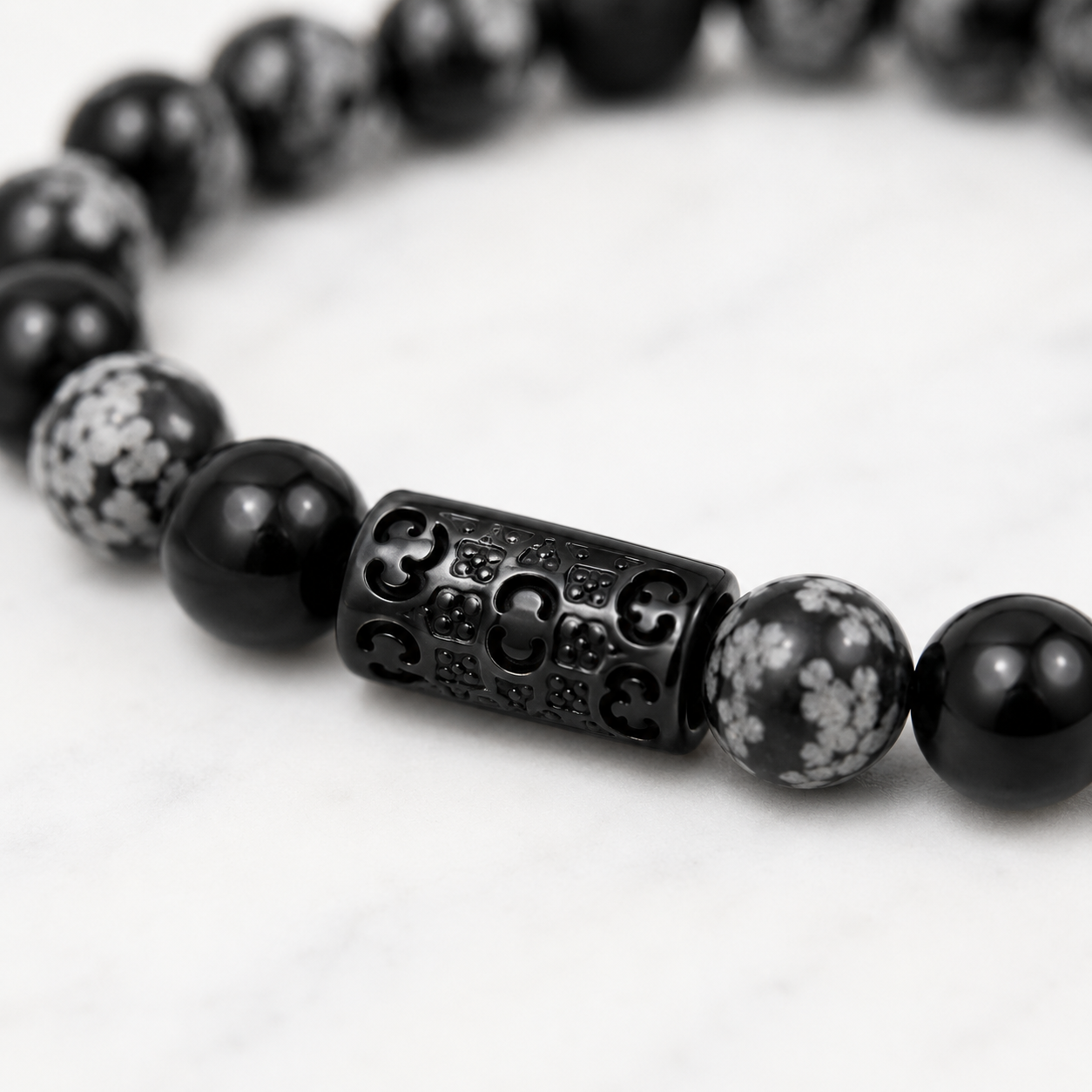 Close-up of the black stainless steel Fleur & Stone signature connector on a Snowflake Obsidian bracelet.