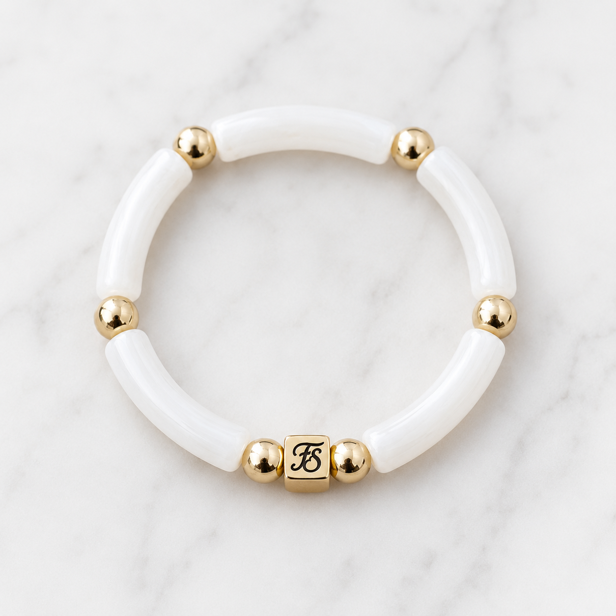 White Dunes Bracelet by Fleur & Stone featuring white acrylic tube beads, polished gold hematite spacer beads and a gold stainless steel logo bead on a white marble background.