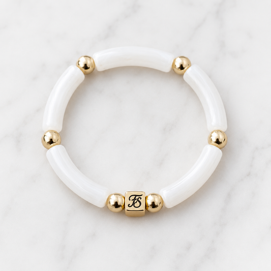 White Dunes Bracelet by Fleur & Stone featuring white acrylic tube beads, polished gold hematite spacer beads and a gold stainless steel logo bead on a white marble background.