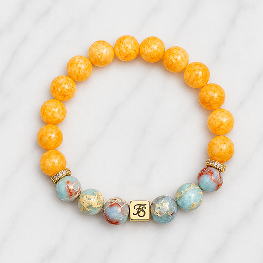 Handcrafted Natural Shoushan Stone and Chinese Yellow Jade stretch bracelet featuring 10mm Shoushan Stone beads, 10mm Chinese Yellow Jade centre beads, gold plated hematite spacers and a gold stainless steel Fleur & Stone logo bead on a light white marble background.